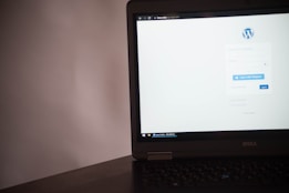 A laptop displaying a login page for a WordPress site. The screen shows fields for username and password, along with options to log in via Telegram or the standard login button. The laptop is positioned on a dark surface with a plain background.