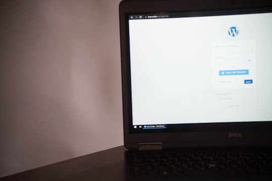 A laptop displaying a login page for a WordPress site. The screen shows fields for username and password, along with options to log in via Telegram or the standard login button. The laptop is positioned on a dark surface with a plain background.