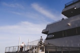 A large cruise ship is docked, featuring a person in uniform standing on the deck near the railing under a clear blue sky. The ship is named 'Odyssey' with its name visible on the side. The scene conveys an atmosphere of anticipation or readiness.