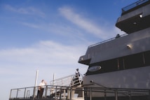 A large cruise ship is docked, featuring a person in uniform standing on the deck near the railing under a clear blue sky. The ship is named 'Odyssey' with its name visible on the side. The scene conveys an atmosphere of anticipation or readiness.
