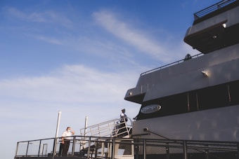 A large cruise ship is docked, featuring a person in uniform standing on the deck near the railing under a clear blue sky. The ship is named 'Odyssey' with its name visible on the side. The scene conveys an atmosphere of anticipation or readiness.