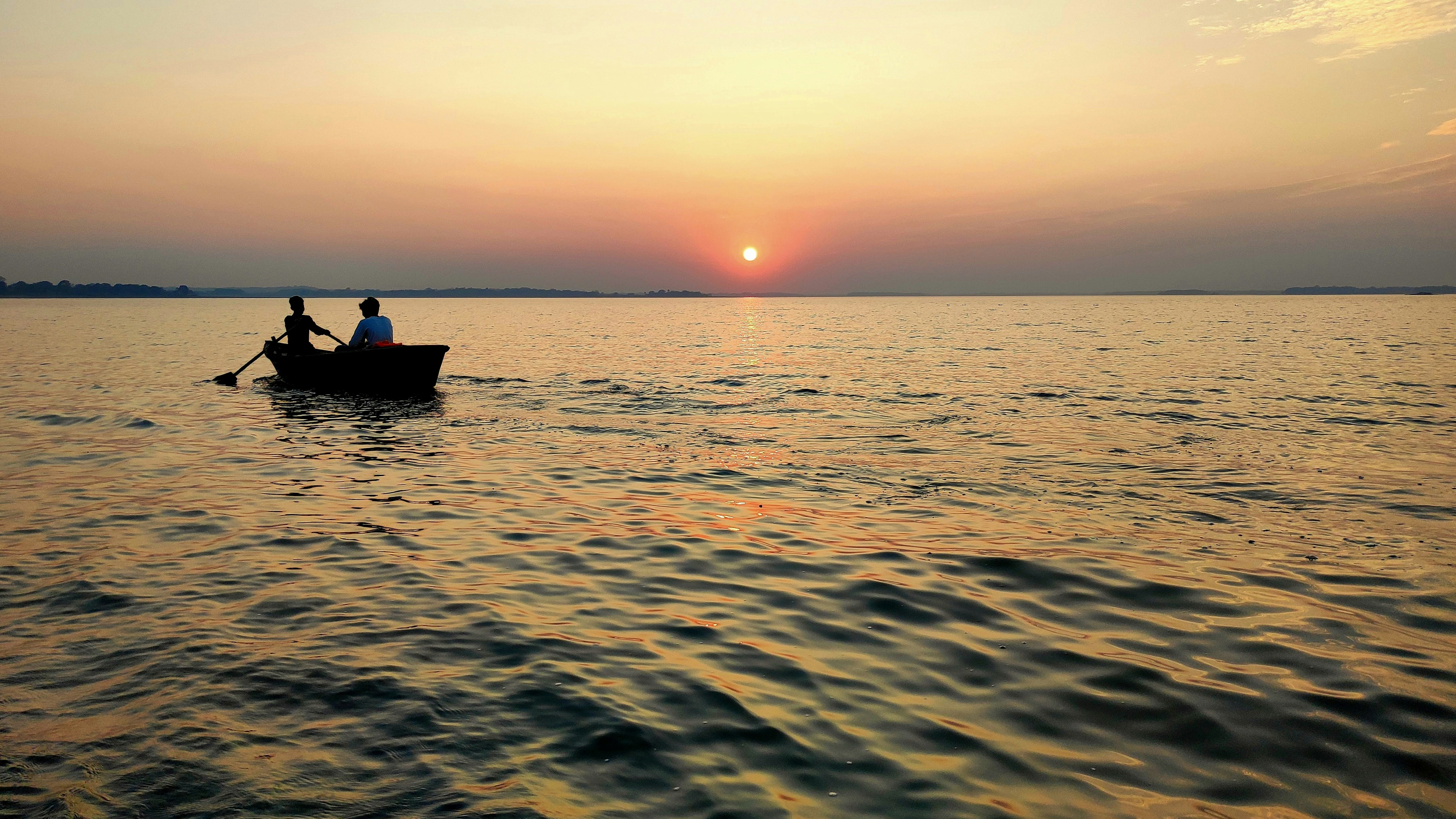 Romantic houseboat on Dal Lake at sunset with golden reflections on water, rose petals on deck, intimate dinner setup