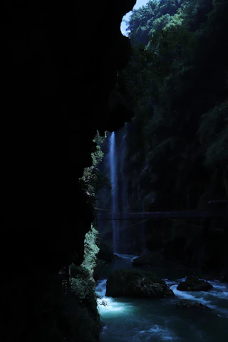 A serene view of the 7-meter waterfall cascading into the river at the edge of the canyon, surrounded by lush greenery.
