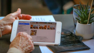 An elderly man smiling as he learns to use a tablet with patient guidance from an expert.