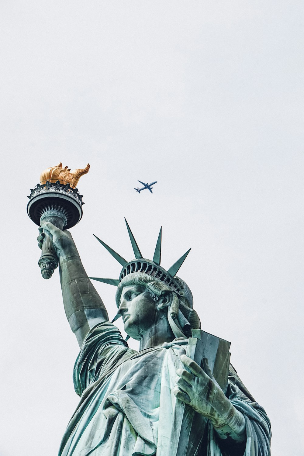 a statue of a person holding a torch and a bird flying in the sky