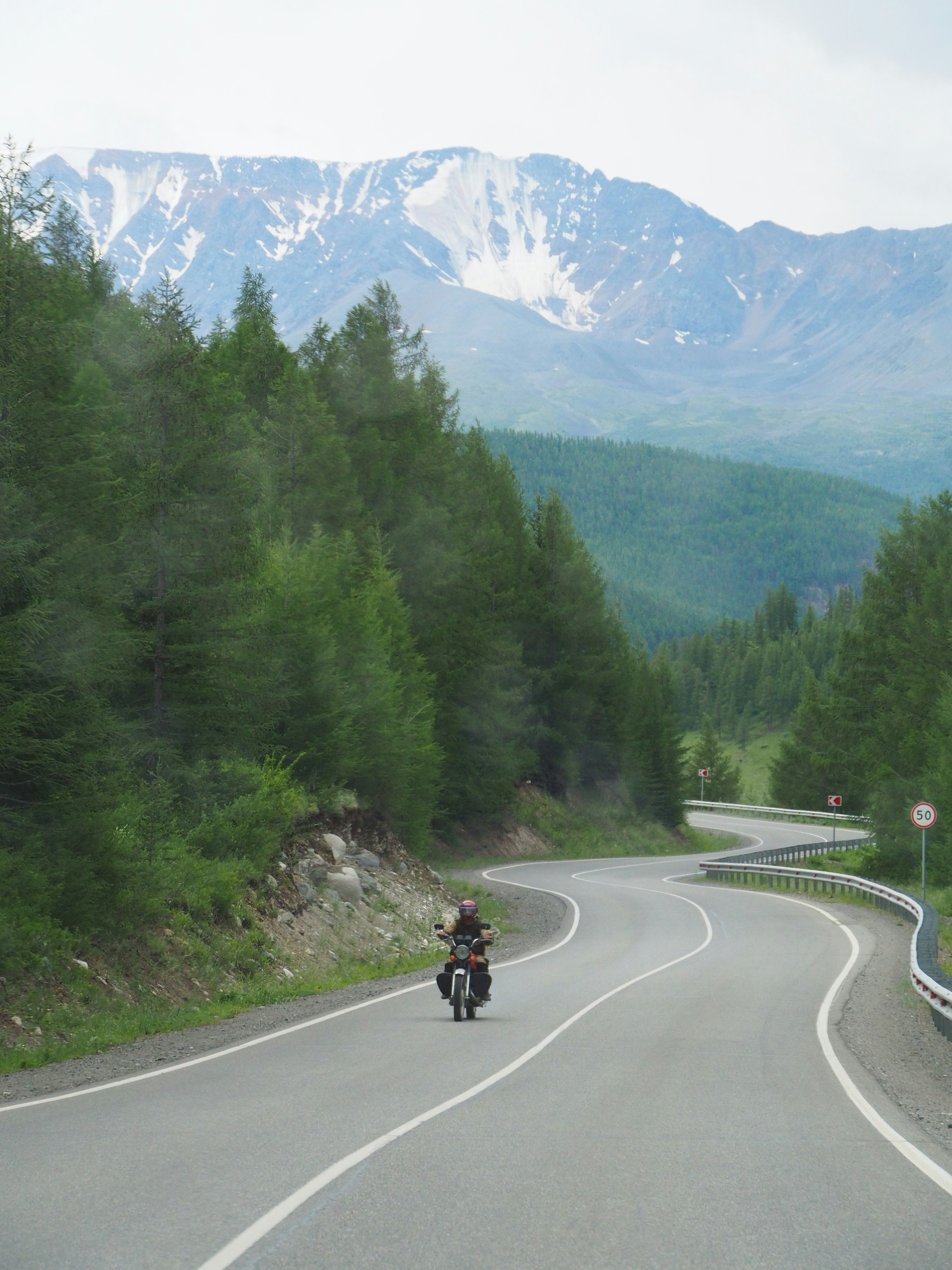 a person riding a motorcycle on a road with trees and mountains in the background