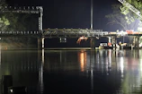 Night view of a bridge under construction illuminated by bright work lights.