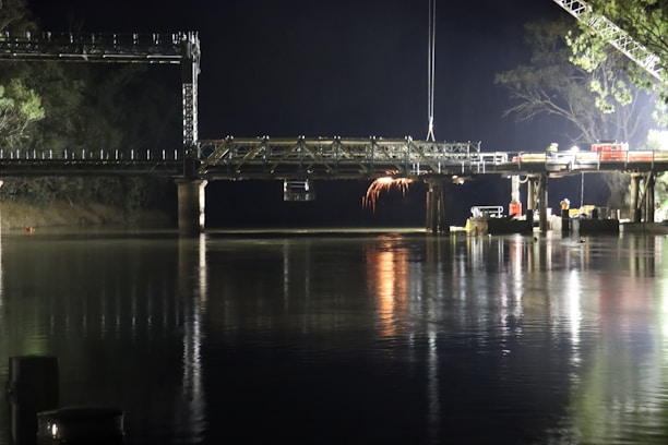 Technicians carefully repairing a bridge's concrete support under bright construction lights.