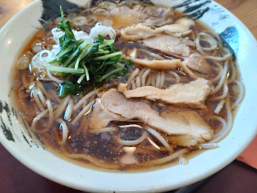A steaming bowl of ramen with rich broth, tender noodles, and vibrant toppings in a rustic ceramic bowl.