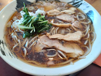 A steaming bowl of ramen with rich broth, tender noodles, and vibrant toppings, served in a minimalist ceramic bowl.