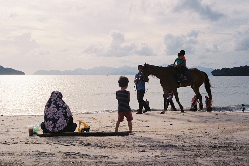a group of people stand on a beach with a horse
