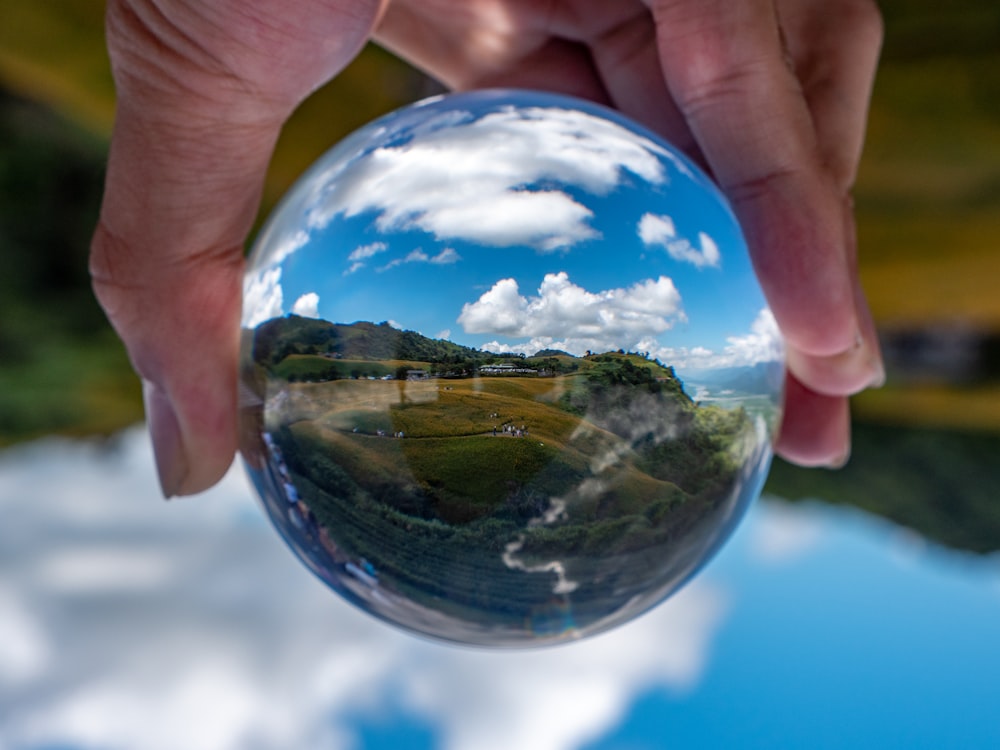 a hand holding a clear sphere with a blue sky and clouds