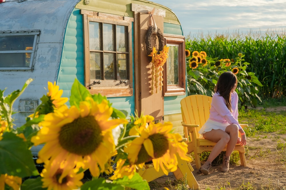 a person sitting on a chair outside a house with sunflowers