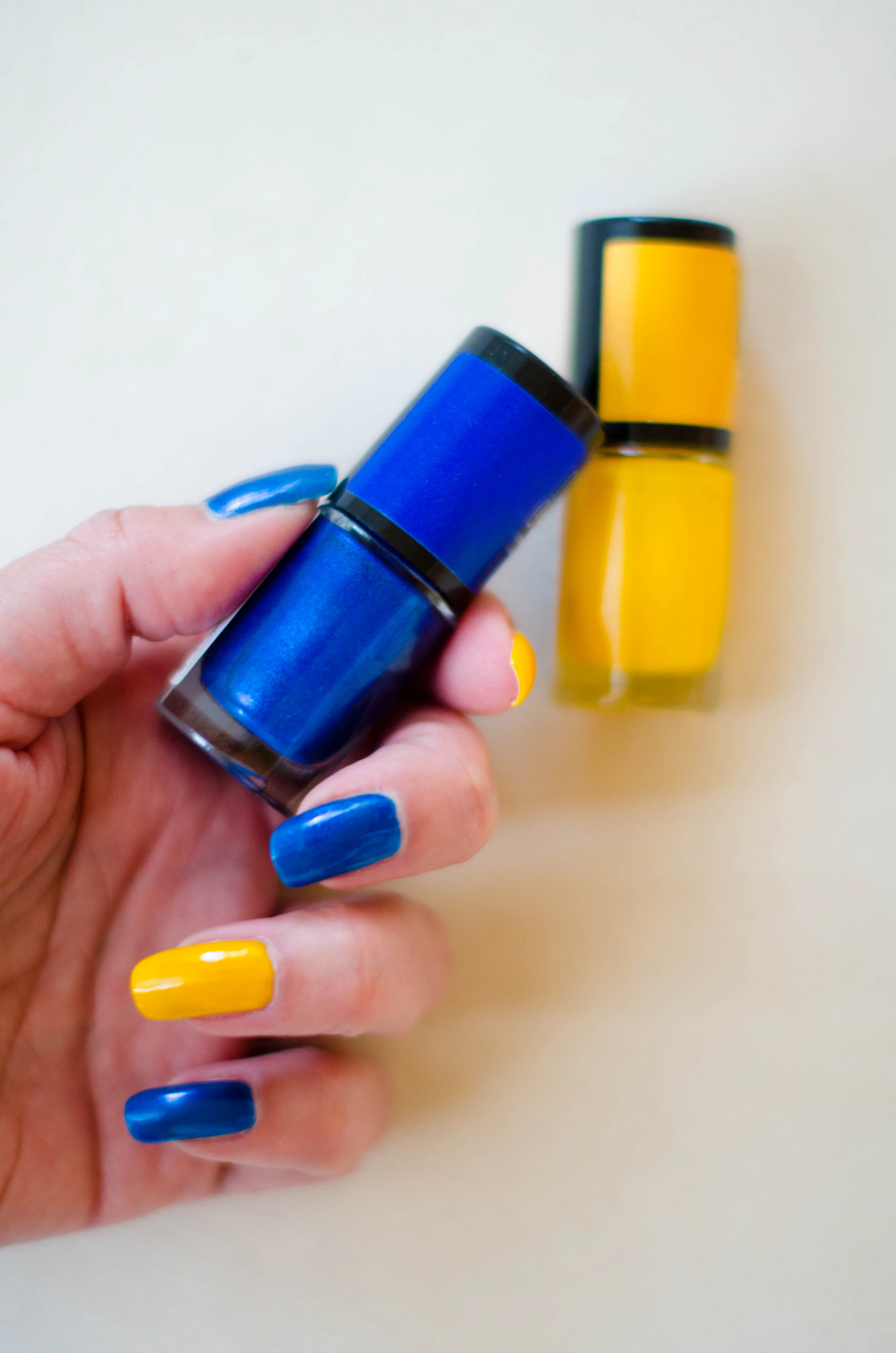 a hand holding a blue and yellow nail polish