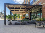 A vibrant outdoor patio rug laid out under a shaded pergola with potted plants.