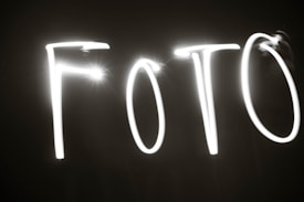 Bright white streaks of light form the letters 'FOTO' against a dark background, creating a striking contrast.