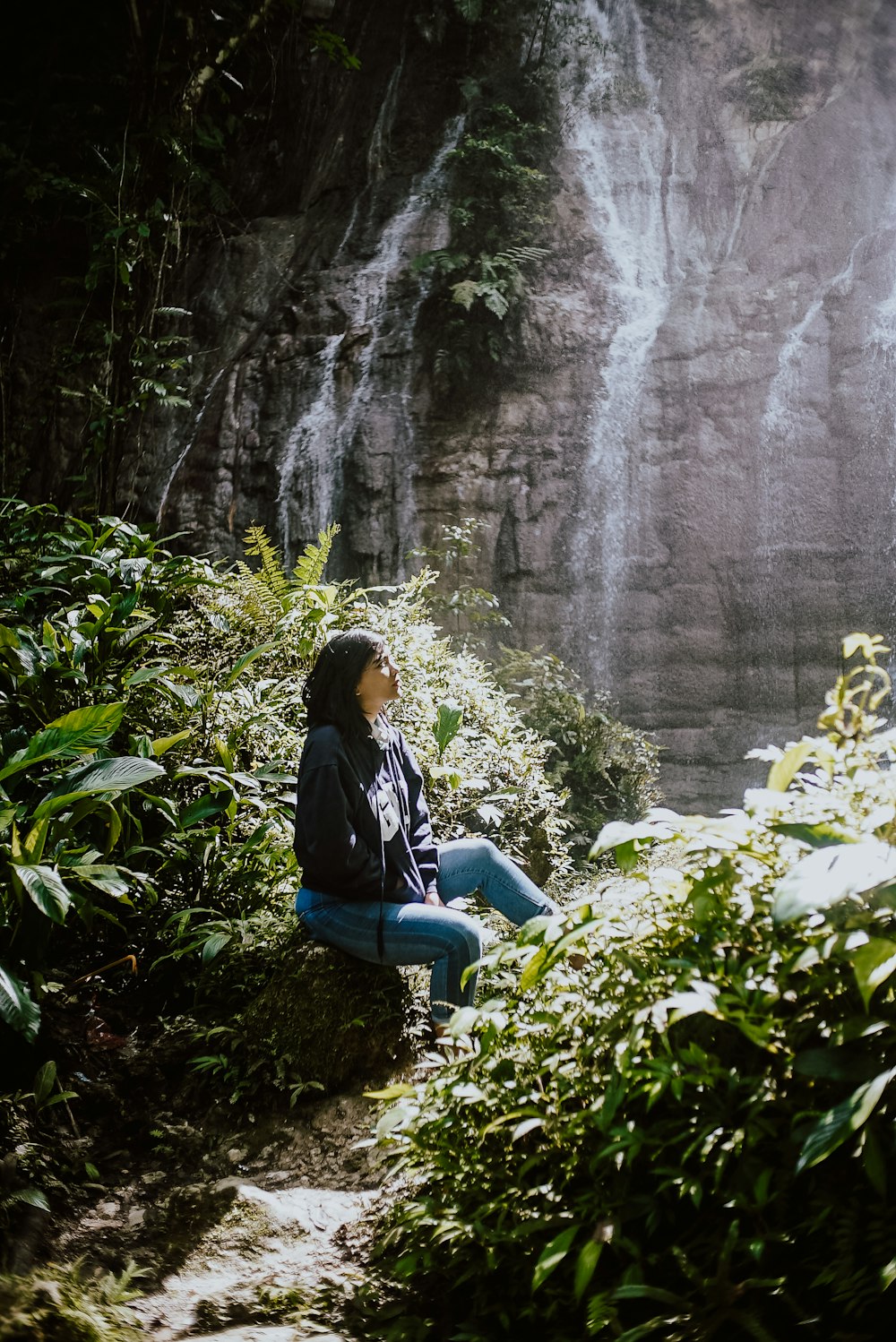 a person sitting on a rock by a waterfall