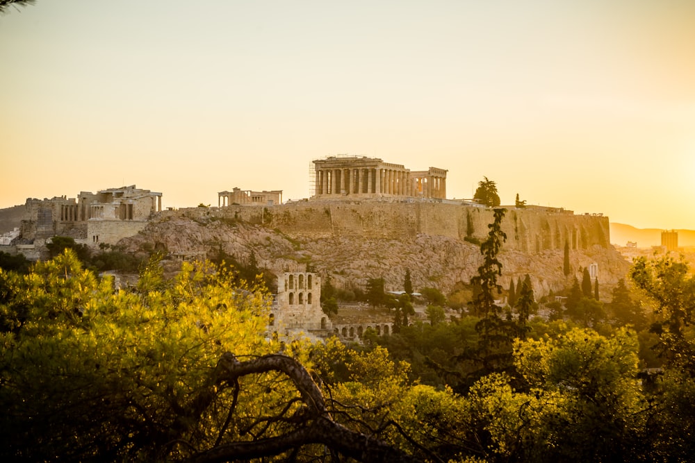 un gran edificio de piedra en una colina con la Acrópolis de Atenas al fondo