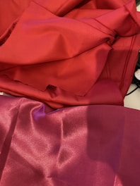 Vibrant red and deep pink fabrics are laid out, creating a smooth and shiny surface with visible folds and creases.