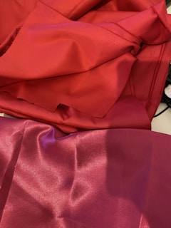 Vibrant red and deep pink fabrics are laid out, creating a smooth and shiny surface with visible folds and creases.
