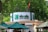A circular kiosk is prominently displayed, featuring the signage 'Bốn Mùa - Four Seasons' in bold green letters. Surrounding the kiosk are several large green umbrellas providing shade. The background is lush with dense green foliage, and a national flag is visible atop the structure.