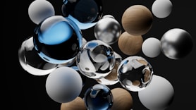 A collection of various spheres, including glass, wooden, and metallic textures, arranged in a dynamic floating composition against a dark background. The spheres reflect and refract light, creating an intricate interplay of shadows and highlights.