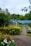 A lush garden with a variety of vibrant flowers in yellow, orange, and purple blooms alongside a gravel path leading to a building with a blue roof. Trees and greenery fill the background, creating a serene and natural setting.