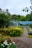 A lush garden with a variety of vibrant flowers in yellow, orange, and purple blooms alongside a gravel path leading to a building with a blue roof. Trees and greenery fill the background, creating a serene and natural setting.