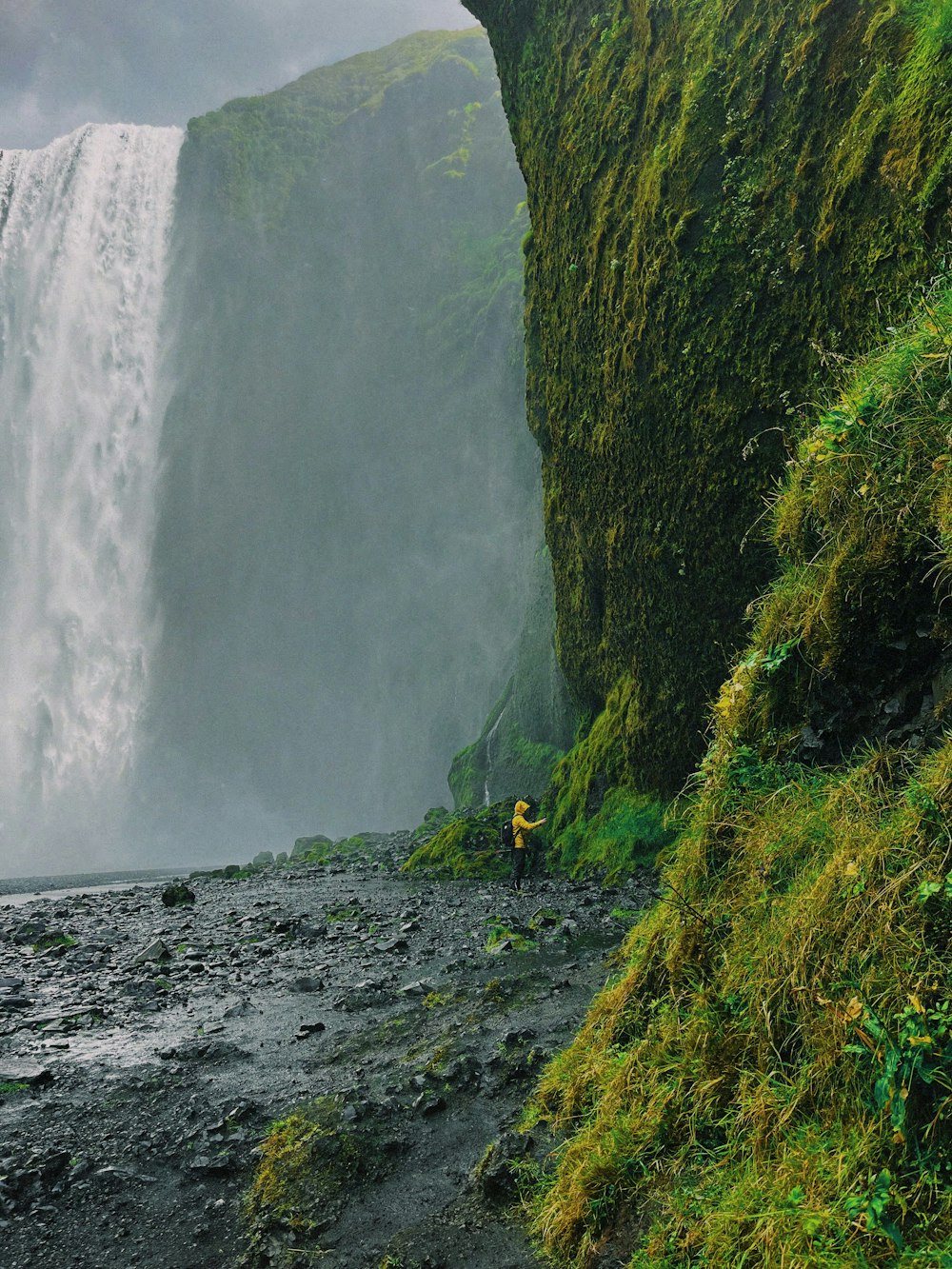 a person hiking on a trail between large waterfalls with Waipio Valley in the background