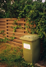 a green garbage can next to a wooden fence