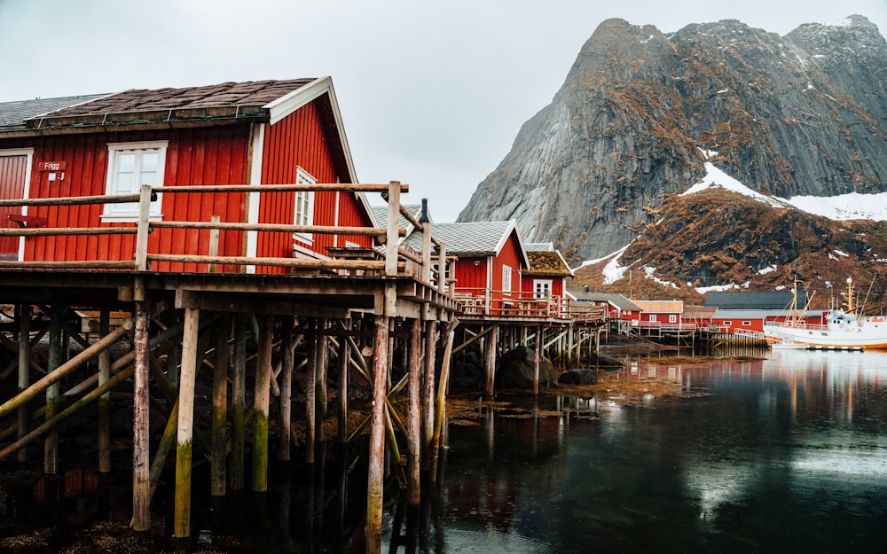 a wooden dock with a red building and mountains in the background
