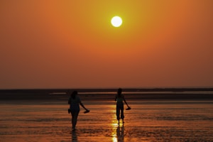 a group of people walking on a beach at sunset