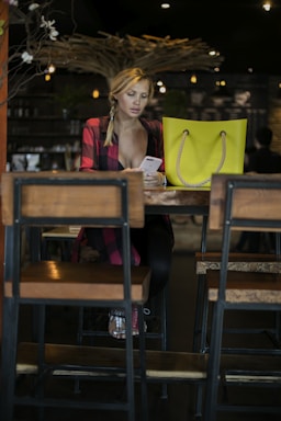 A stylish woman holding a phone, smiling while sitting at a café table.
