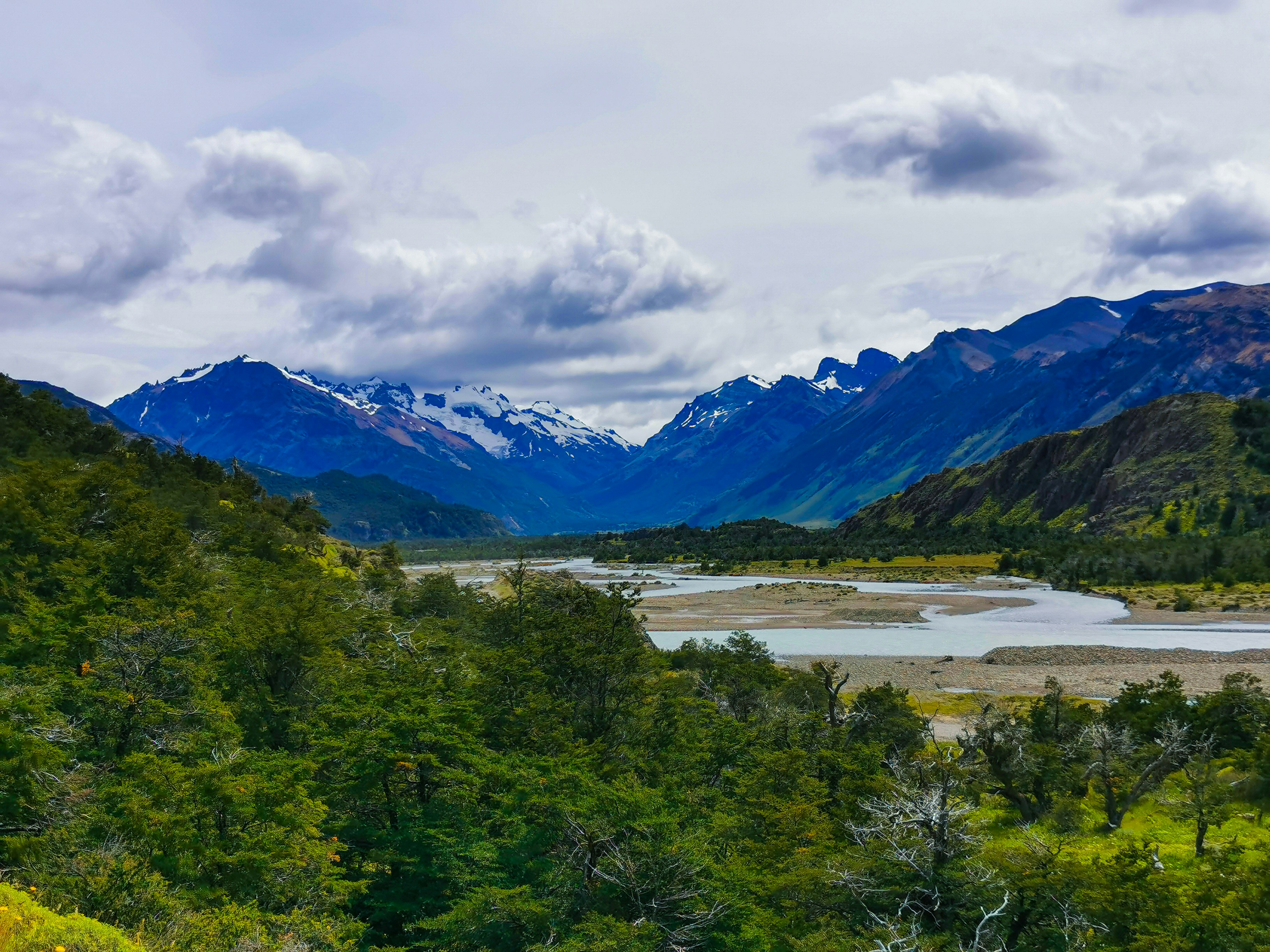 a river running through a valley with mountains in the background, 