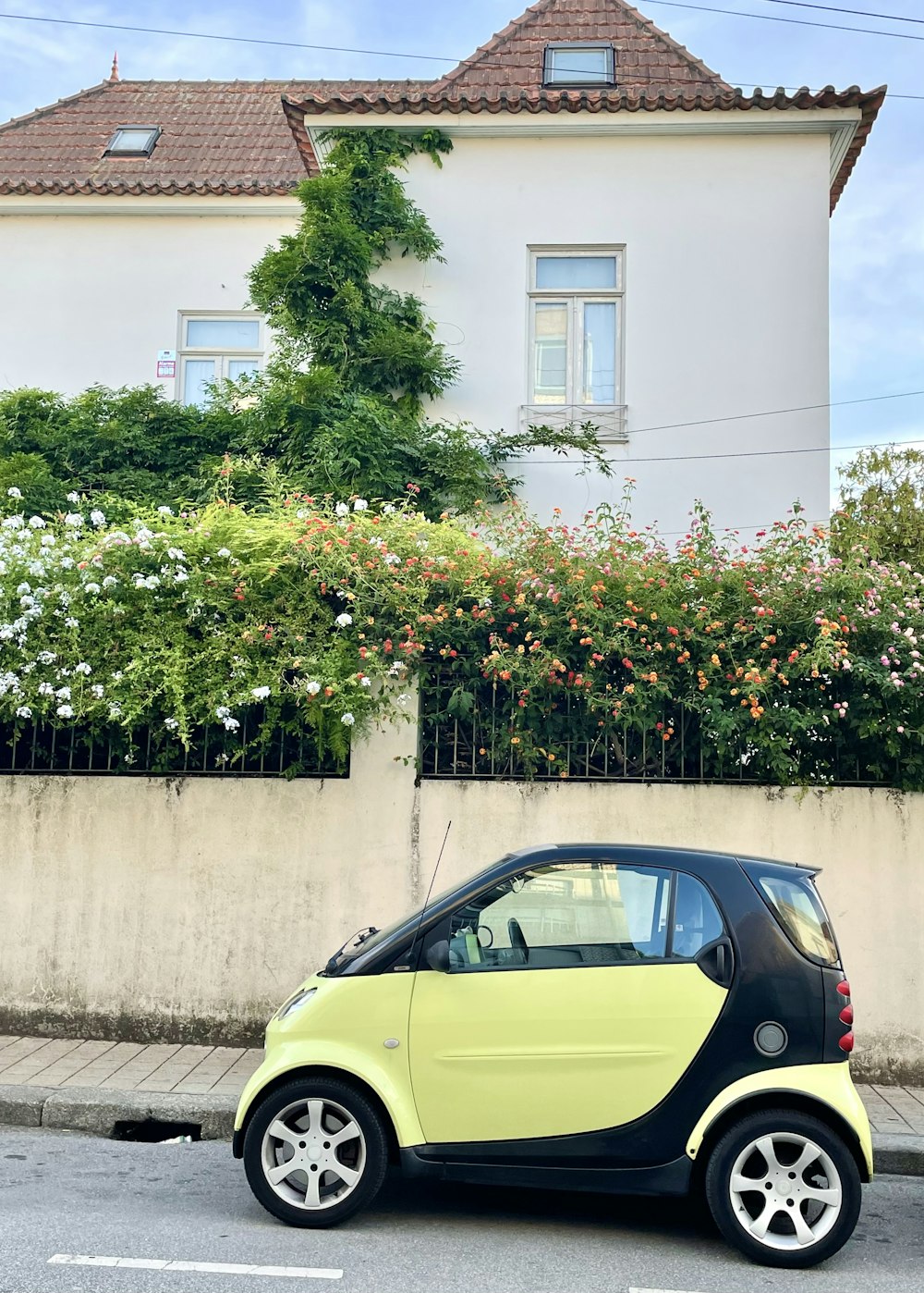 a yellow car parked in front of a house with flowers on the roof