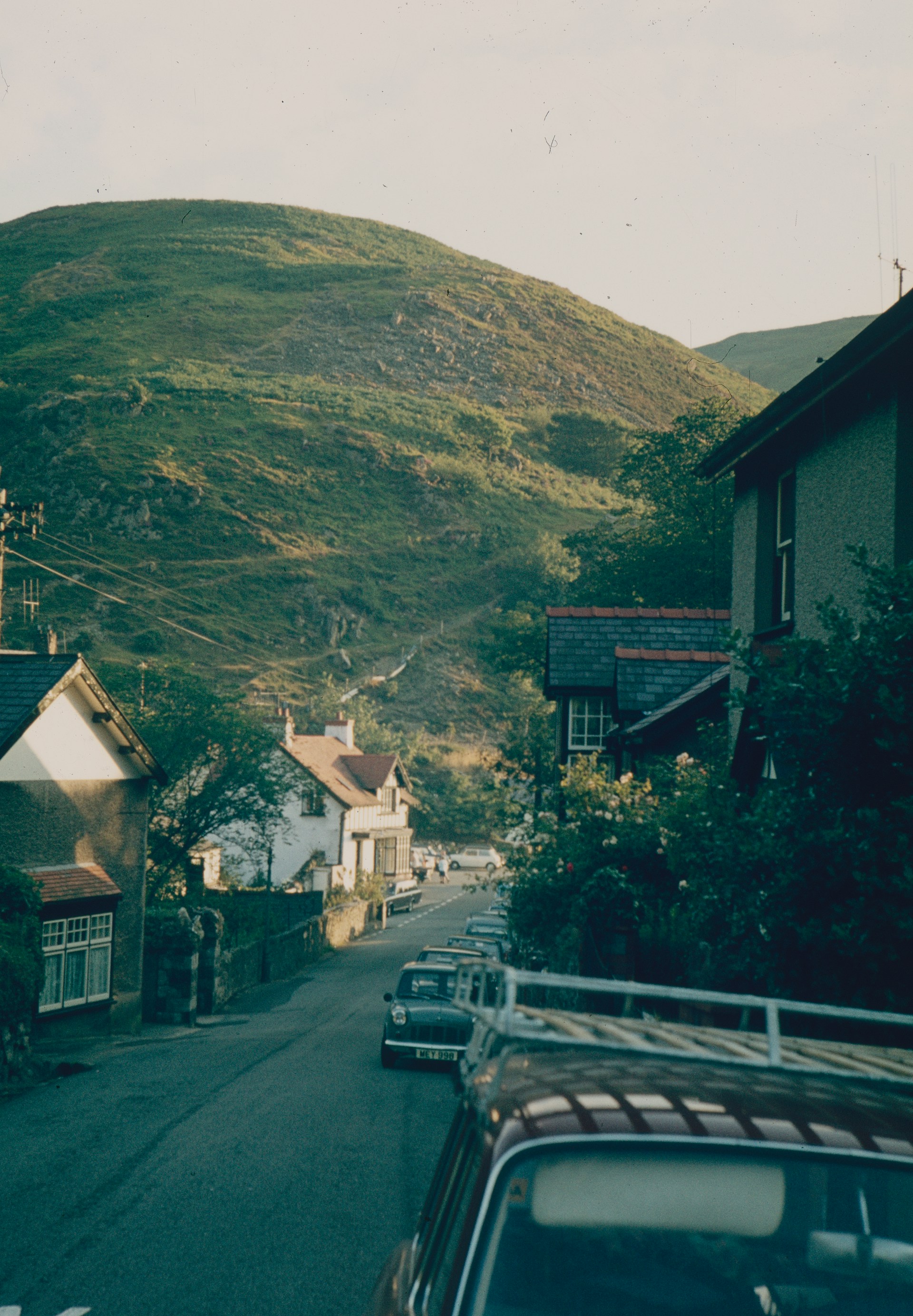 a road with cars and houses on the side and a hill in the background