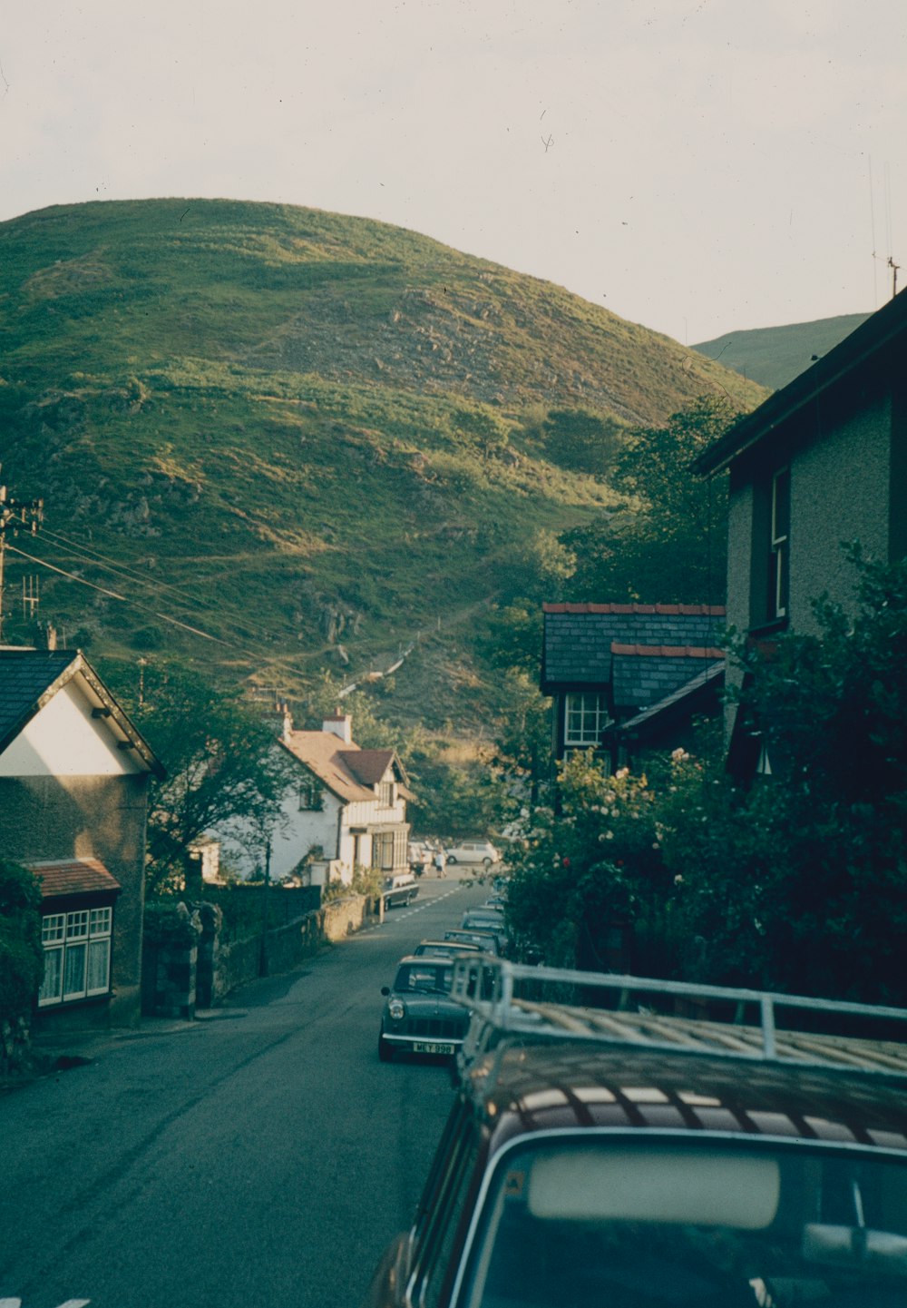 a road with cars and houses on the side and a hill in the background