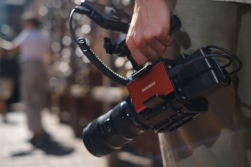 a hand holding a black and red camera