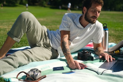a man lying on a blanket with a laptop and a camera