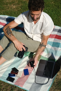 a man sitting on the grass with a laptop and a camera