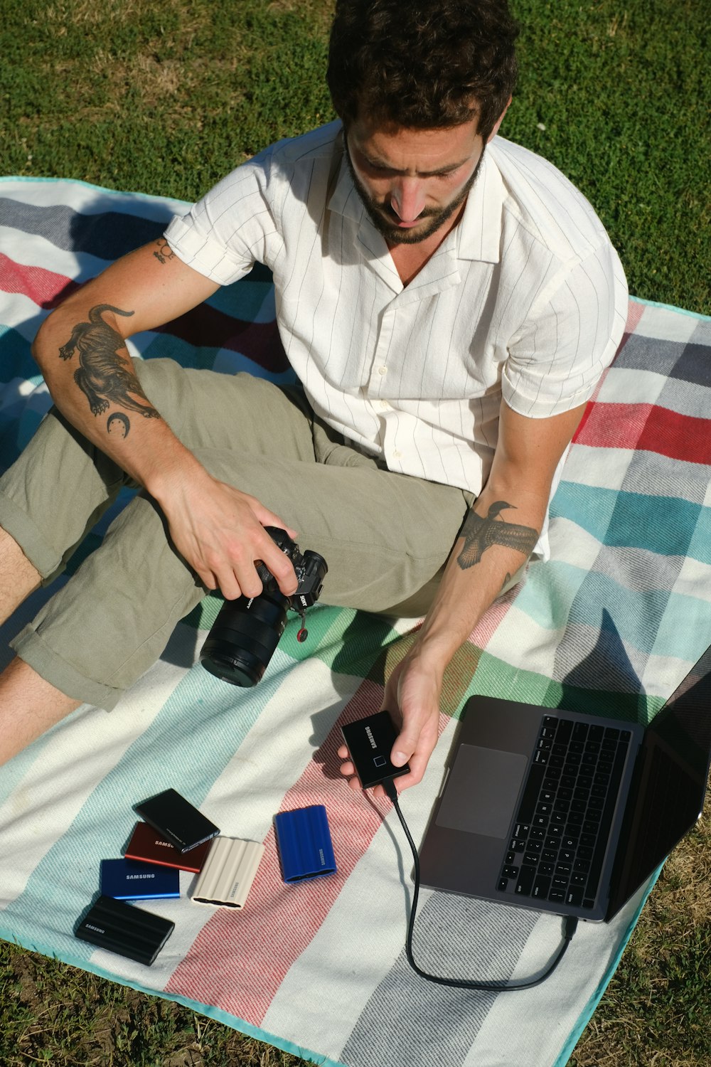 노트북과 카메라를 들고 잔디에 앉아 있는 남자