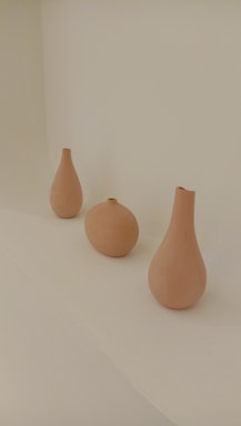 Three ceramic vases are arranged in a row on a plain light background. Each vase has a different shape, featuring smooth curves and a matte finish.