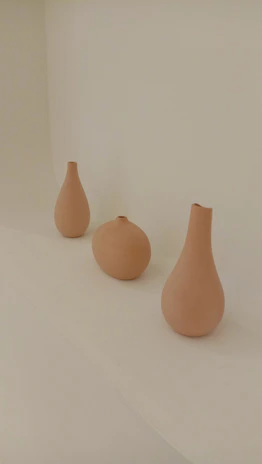 A set of three 3D designed vases arranged on a wooden table, each with a different warm color palette.