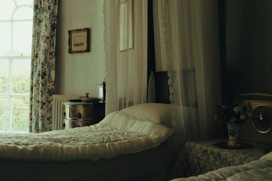 Chambre ancienne, lit double et fenêtre à rideaux ouvrant sur la verdure