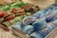 Colorful, sugar-coated gummies are displayed in a bin at a store. The image prominently features two varieties of gummies: blue raspberry-flavored in the foreground and a more assorted green and red variety in the background. Each piece is circular with a sugary texture clearly visible.