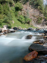 A serene mountain stream flowing through lush green Uttarakhand hills with traditional terraced farms in the background.