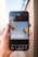 A smartphone held in a hand displays an image editing application featuring a design with two colorful hot air balloons and the phrase 'let's get creative' on a light blue background. The app interface shows various editing options at the bottom, such as styles, text, shapes, and more.