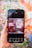 A hand holding a smartphone displaying an image of pink macarons and raspberries with text reading 'Love at First Bite.' The screen shows various editing options at the bottom, including styles, text, shapes, and elements. The background is a colorful, blurred mural with floral patterns.