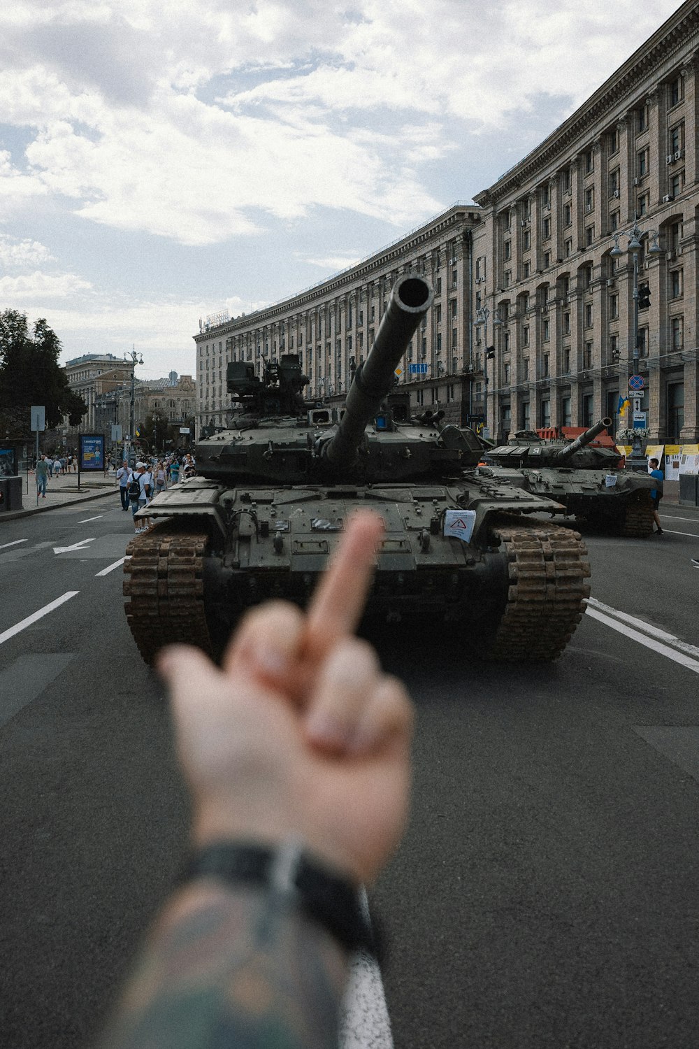 a hand with a gun in front of a military tank on a street