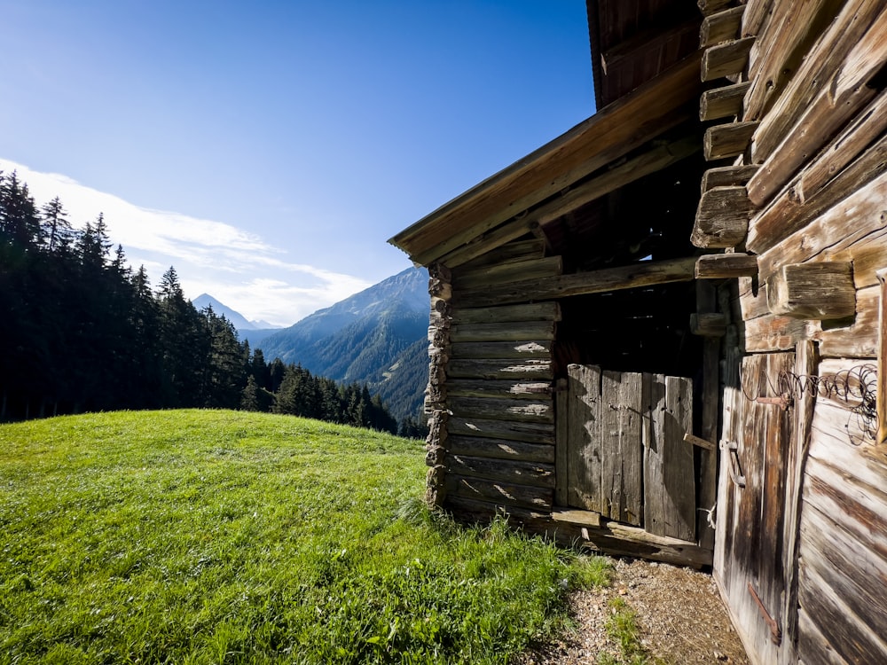 a wooden building with a grass field and mountains in the background